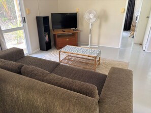 A living room with a sofa, a television, a stand fan, and a small table.