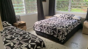 A bedroom with two single beds, a large bed with a floral bedspread, a bedside table with a lamp, and a window with curtains.