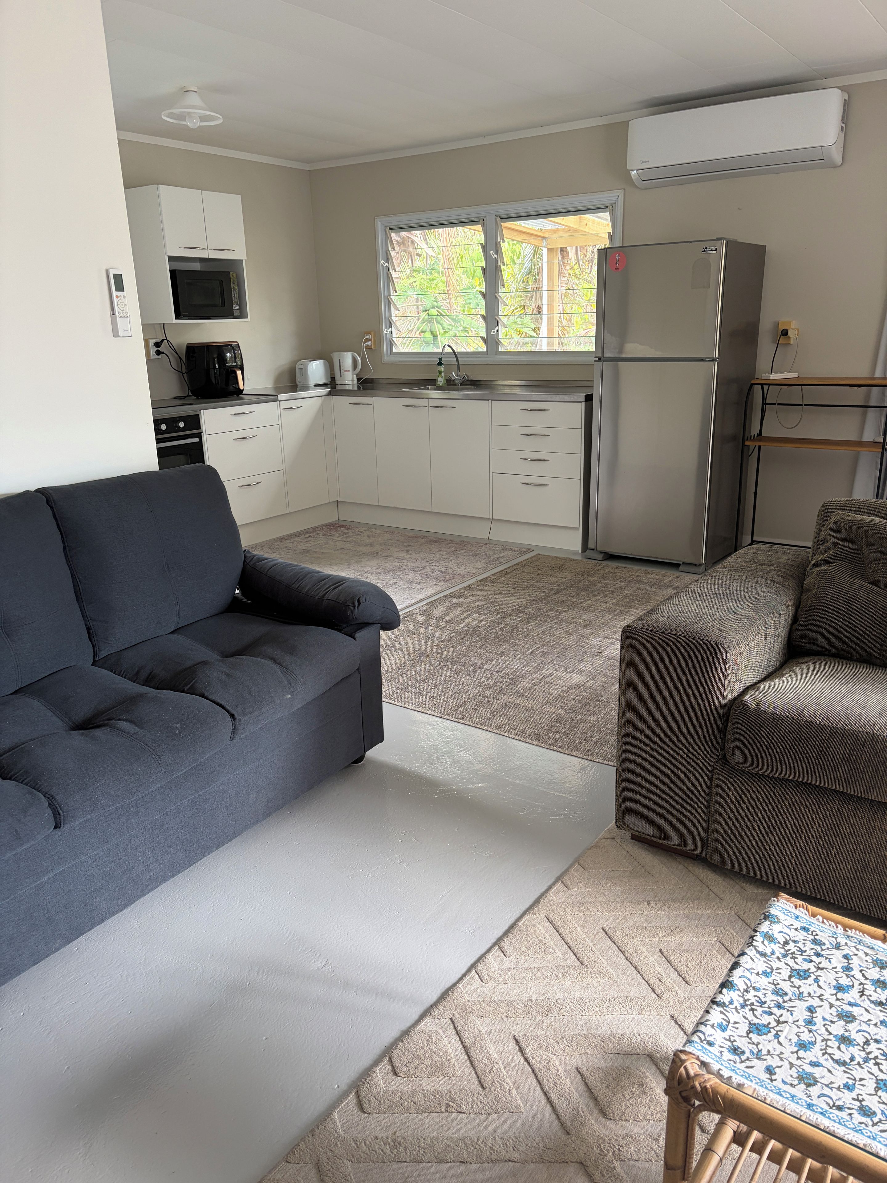 Ein gemütlicher, kompakter Wohnraum mit Sofa, kleinem Tisch, Küchenzeile und Fenster.