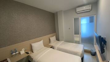 A hotel room with two beds, a desk with a phone and water bottles, an air conditioning unit, and a TV.