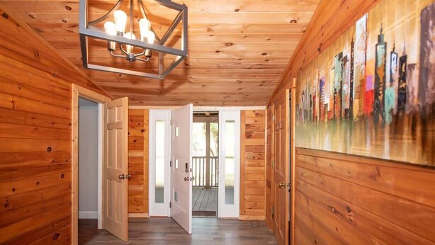 Interior de madera con un pasillo que conduce a una puerta abierta, un aplique de techo y un mural de paisaje urbano en la pared.