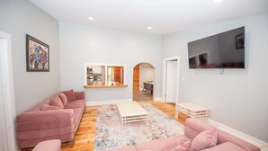 Una sala de estar con un sofá rosa, una mesa de centro y un televisor montado en la pared.