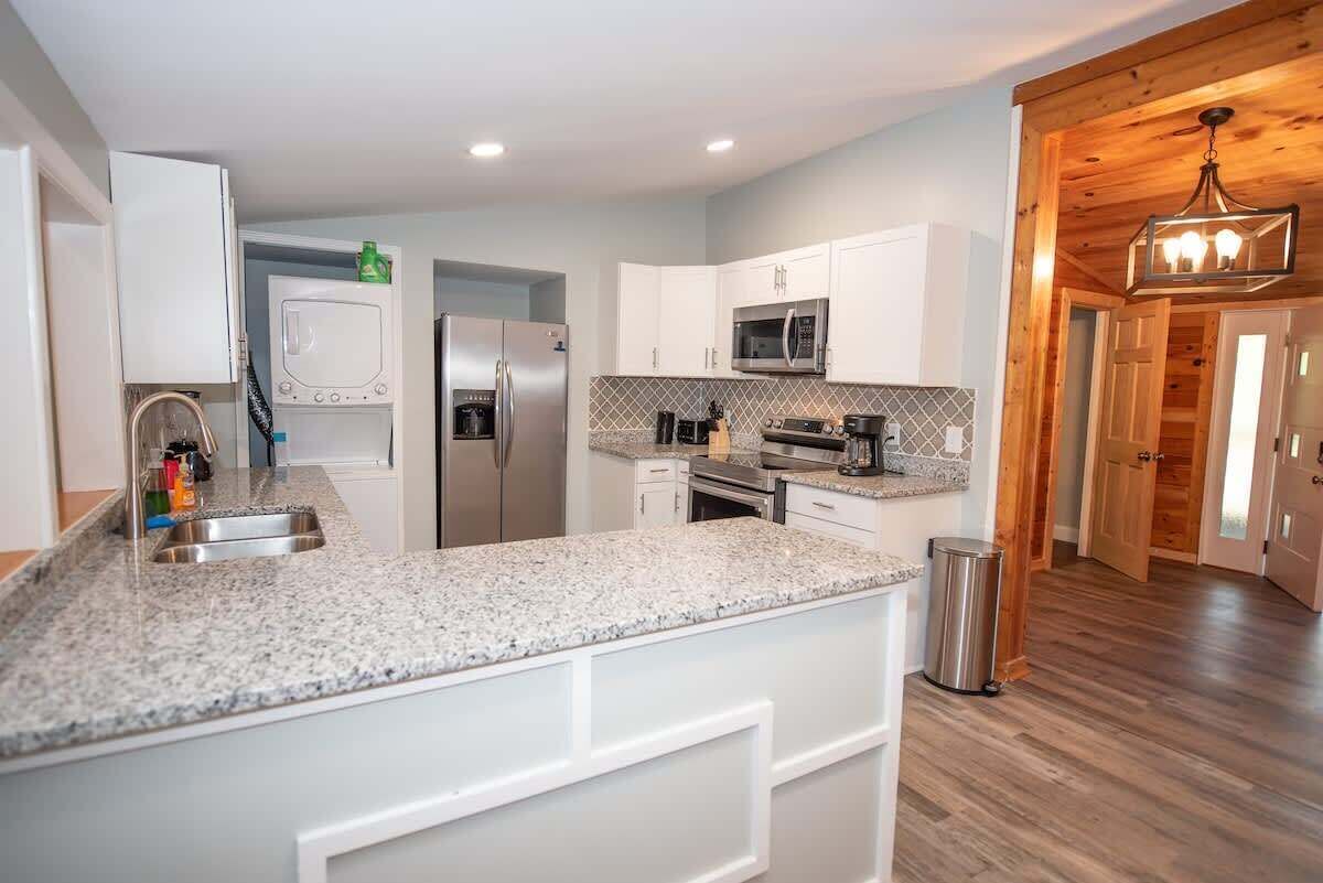 A modern kitchen with white cabinetry, granite countertops, stainless steel appliances, and a wooden floor.