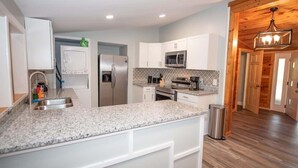 Una cocina moderna con armarios blancos, encimeras de granito, electrodomésticos de acero inoxidable y suelo de madera.