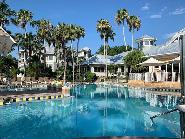Relax by the resort pool surrounded by palm trees and lounge chairs.