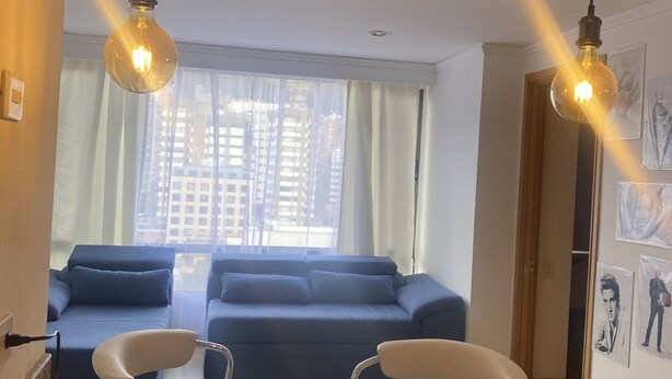 Un salon moderne avec un canapé bleu, un coin repas doté d’un comptoir en granit et deux lampes suspendues.