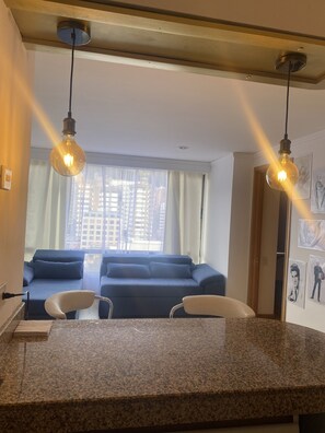 Een moderne woonkamer met een blauwe bank, een eetgedeelte met een granieten aanrechtblad, en twee hangende lampen.