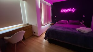 Une chambre avec un lit, un bureau et une chaise. Il y a un panneau lumineux au néon sur le mur.