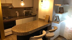 Une cuisine dotée de plans de travail en granit, d’un four encastré, d’un micro-ondes et d’un évier. On y trouve deux luminaires suspendus, un tableau encadré au mur et une petite étagère sur laquelle est posé un objet décoratif encadré.