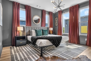 A modern bedroom with a large bed, a round mirror, and a view of the sky through the window.