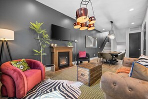 A modern living room with a fireplace, a red armchair, a wooden coffee table, and a staircase leading to another level.
