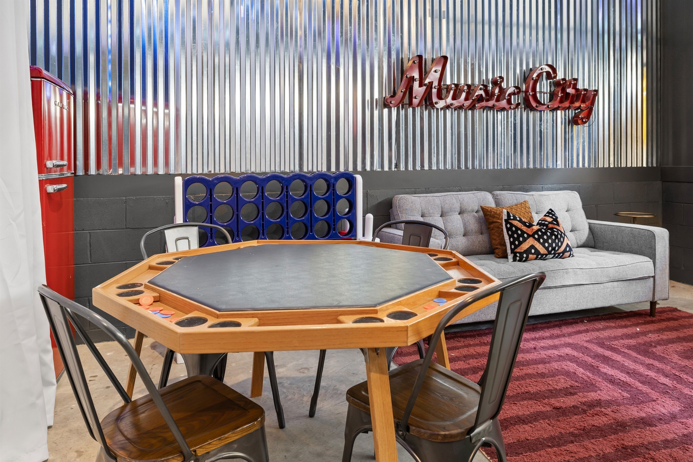 A room with a round table, chairs, a sofa, and a wall with vertical stripes and a 'Music City' sign.