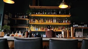 Baarialue, jossa on hyllyjä täynnä pulloja ja laseja, tiski ja baarituoleja.