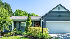 Une maison à deux étages avec un garage, un porche à l’avant et un jardin bien entretenu.