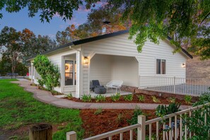 Uma casa térrea com varanda coberta, chaminé de tijolos e um pequeno jardim com plantas e um caminho.