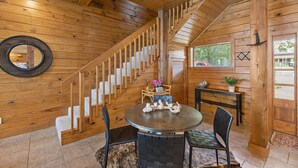 Un intérieur en bois avec un escalier, une table ronde entourée de chaises et une porte dotée d’une fenêtre.