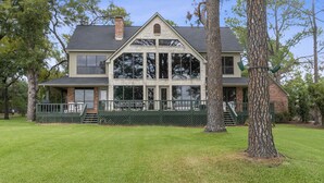Une maison à deux étages avec une grande véranda à l’avant, une cheminée en briques et une pelouse bien entretenue.