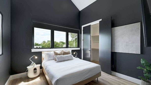 A modern bedroom with a large bed, a bedside table, a lamp, a window, and a wall-mounted TV. - Pool, Hot Tub | Spacious Holiday Retreat for 14 (Austin)