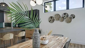A modern dining area with a wooden table, wicker chairs, a large potted plant, and decorative wall art. - Pool, Hot Tub | Spacious Holiday Retreat for 14 (Austin)