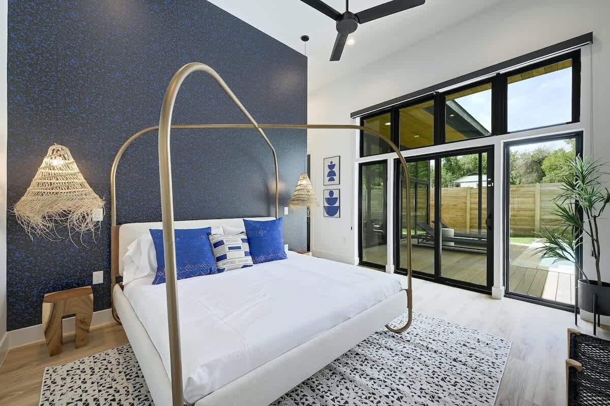 A bedroom with a four-poster bed, large windows, and a ceiling fan.