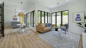 A spacious living area with a sofa, a dining table with chairs, and a large window providing a view of the outdoors. - Pool, Hot Tub | Spacious Holiday Retreat for 14 (Austin)