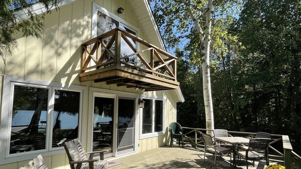 A wooden deck with outdoor furniture, a covered patio, and a view of a body of water. - Waterfront, peaceful, cozy, cottage w/dock amazing sunsets, kayaks,3 bed/2 bath. (Lake Leelanau)
