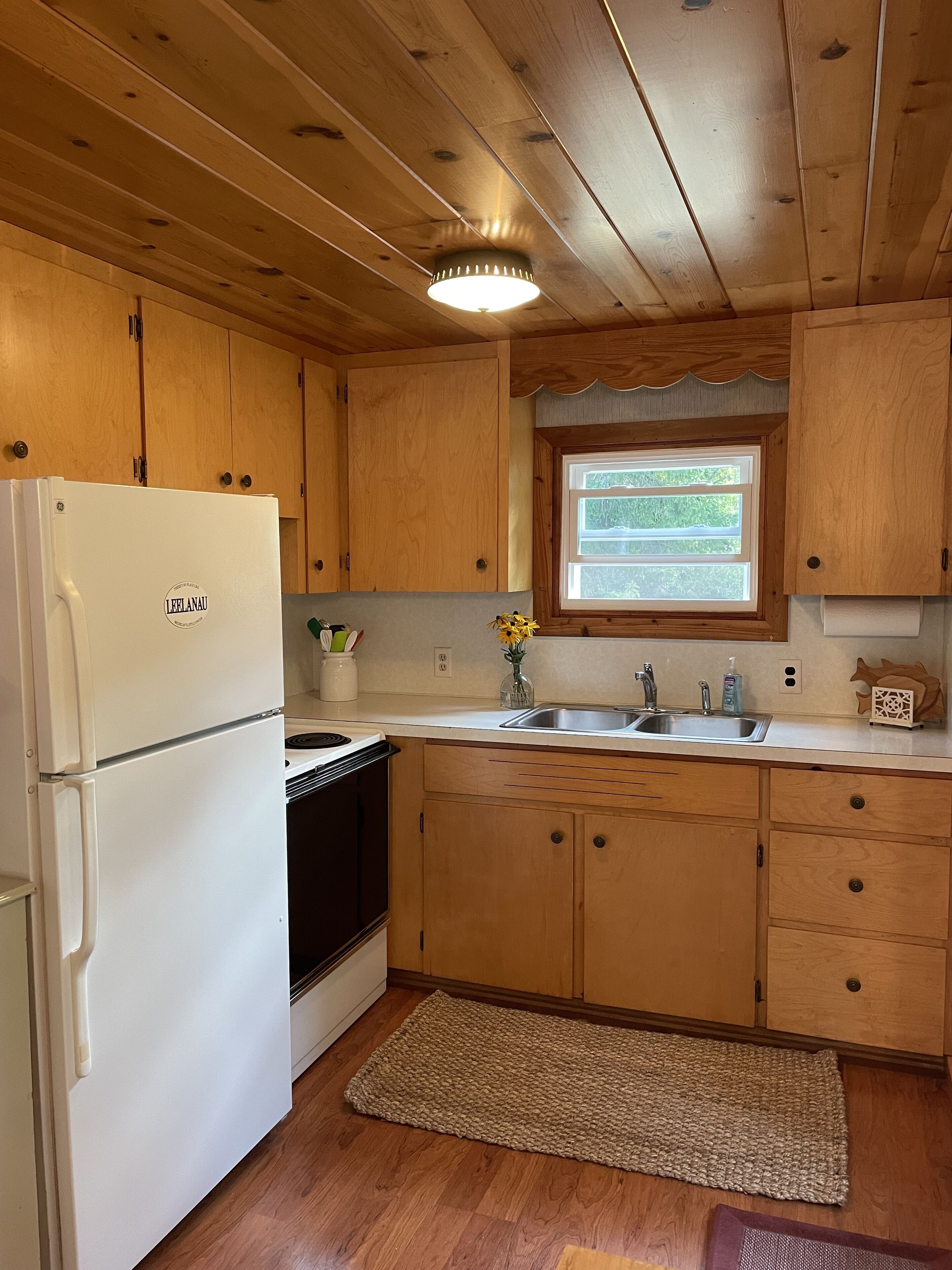 A kitchen with wooden cabinets, a white refrigerator, a window, and a sink.