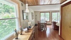 A spacious kitchen with wooden floors, large windows, and a dining area with a table and chairs. - Waterfront, peaceful, cozy, cottage w/dock amazing sunsets, kayaks,3 bed/2 bath. (Lake Leelanau)