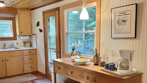 A kitchen with wooden cabinets, a wooden countertop, a hanging light fixture, a window, and a framed picture on the wall. - Waterfront, peaceful, cozy, cottage w/dock amazing sunsets, kayaks,3 bed/2 bath. (Lake Leelanau)