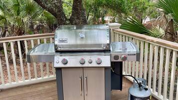 A portable gas grill with a propane tank on a wooden deck.