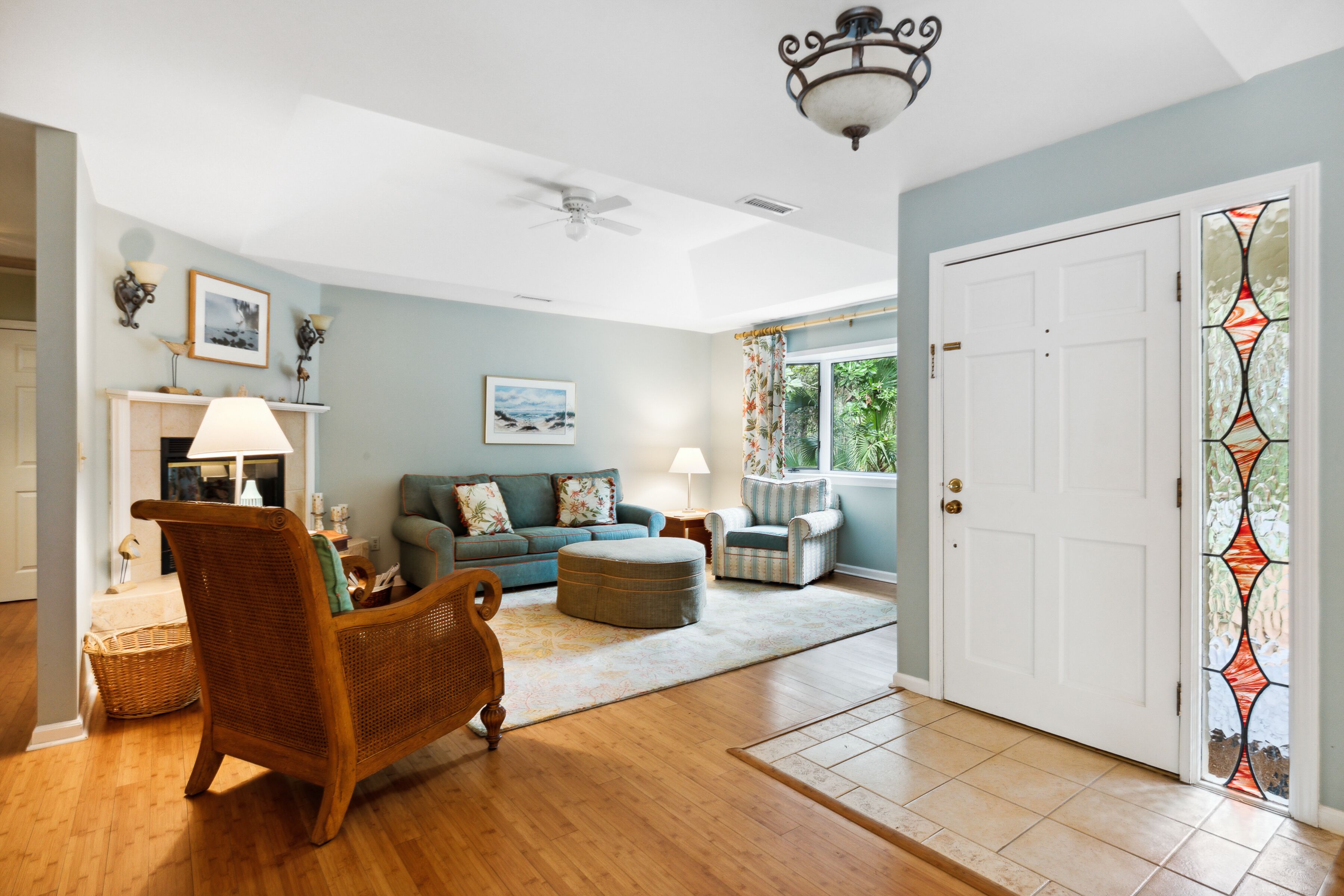 A spacious living room with a wooden floor, a rattan chair, a sofa, and a dining table.