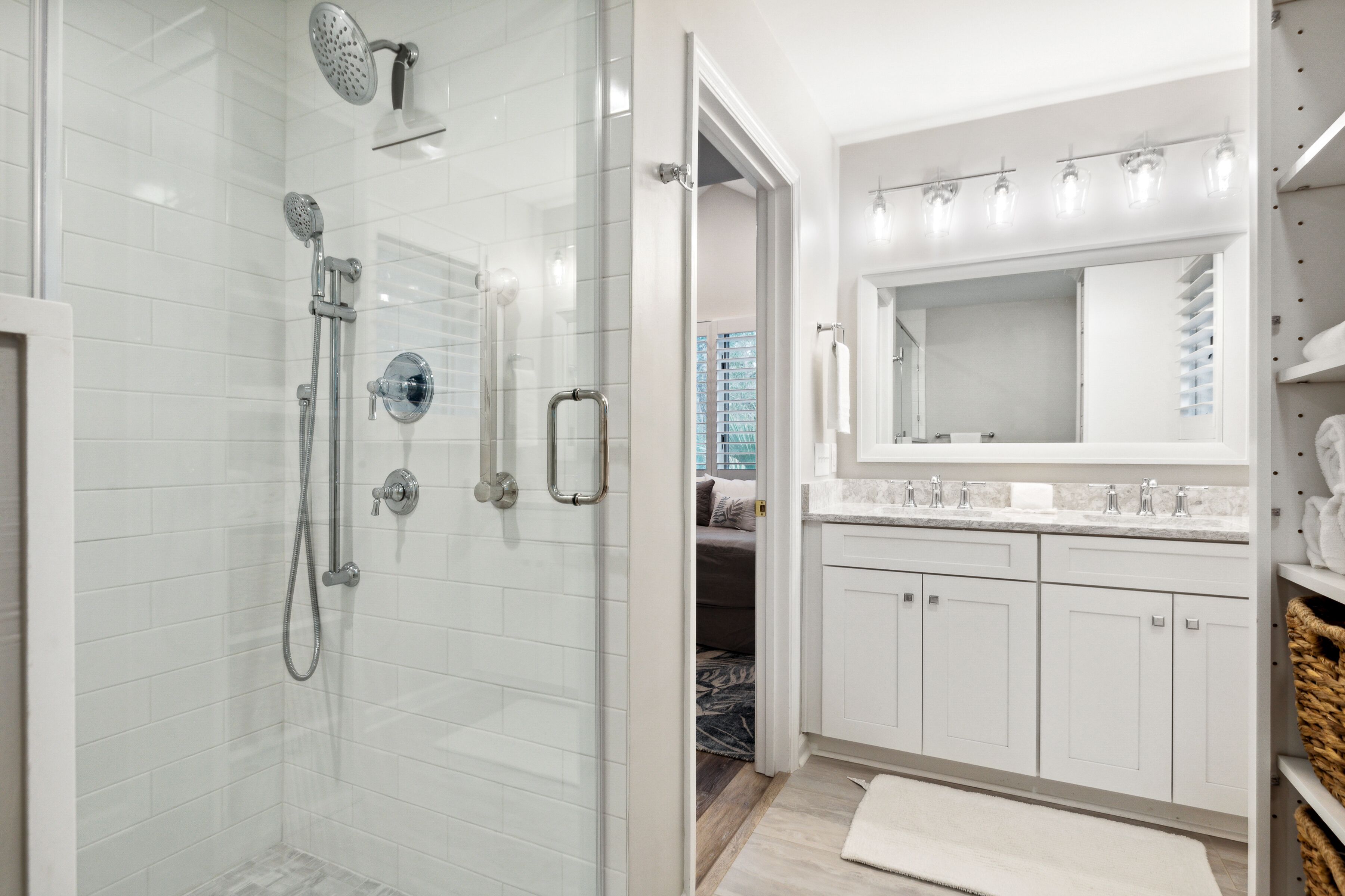 A modern bathroom with a glass-enclosed shower, white tiled walls, a large mirror above the sink, and a walk-in closet with white cabinets.