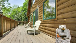 Puuinen mökki, jossa on kuisti, kaksi Adirondack-tyylistä puutarhatuolia ja karhupatsas.