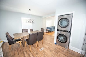 Eine moderne Küche mit integriertem Wasch- und Trockner, einem Essbereich mit Holztisch und -stühlen sowie ein Wohnzimmer mit blauem Sofa.