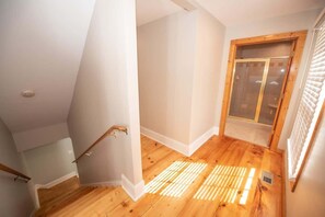 Ein Eckzimmer mit Holzboden, Holztür und einem Fenster mit Jalousien.