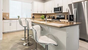 A modern kitchen with white cabinets, stainless steel appliances, and a central island with bar stools.