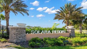 A sign for Solara Resort with a stone wall, palm trees, and a clear sky.