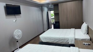 A hotel room with two beds, a TV mounted on the wall, a ceiling fan, and a wardrobe.