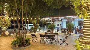 An outdoor patio area with tables and chairs, surrounded by potted plants and string lights.