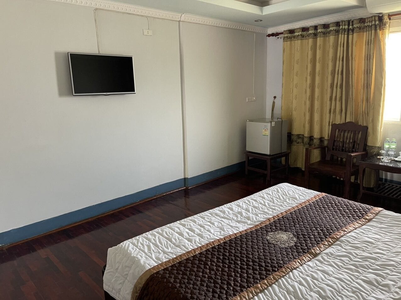 Une chambre d’hôtel avec un lit, un téléviseur à écran plat fixé au mur, une petite table avec une chaise et une fenêtre avec des rideaux.