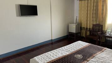 Une chambre d’hôtel avec un lit, un téléviseur à écran plat fixé au mur, une petite table avec une chaise et une fenêtre avec des rideaux.