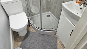 A bathroom with a toilet, a shower with a glass door, and a sink with a soap dispenser. - Town Centre Studio - Sleeps 2 - Parking (Reading)