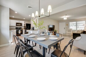 Una cocina moderna con armarios blancos, microondas y comedor con una mesa gris para cuatro.