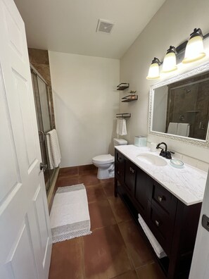 Un baño con inodoro blanco, lavamanos con espejo y zona de ducha.