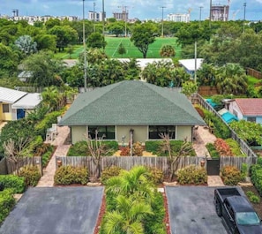 A single-story house with a green roof, surrounded by a fence and lush greenery.