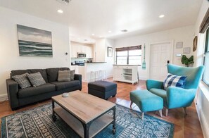 A modern living room with a sofa, ottoman, and armchair, a coffee table, and a kitchen in the background. - ⭐️Beautiful Duplex in Victoria Park!⭐️ (Fort Lauderdale)