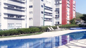 Un bâtiment moderne à plusieurs étages, doté d’une piscine et d’un espace aménagé avec des chaises longues.