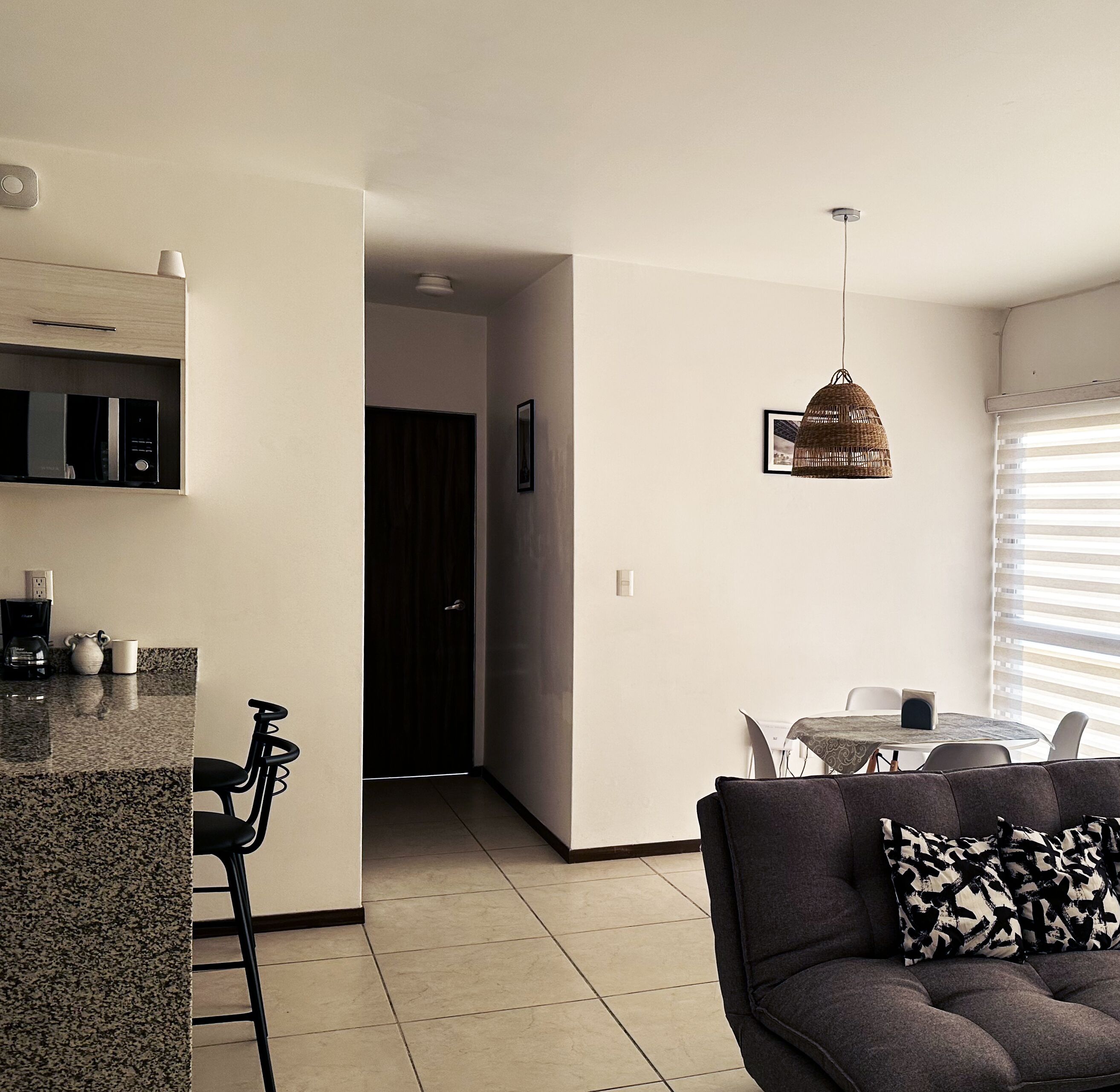 Eine moderne Küche mit integrierten Geräten, ein Essbereich mit rundem Tisch und Stühlen sowie ein Wohnzimmer mit Sofa und einem gemusterten Zierkissen.