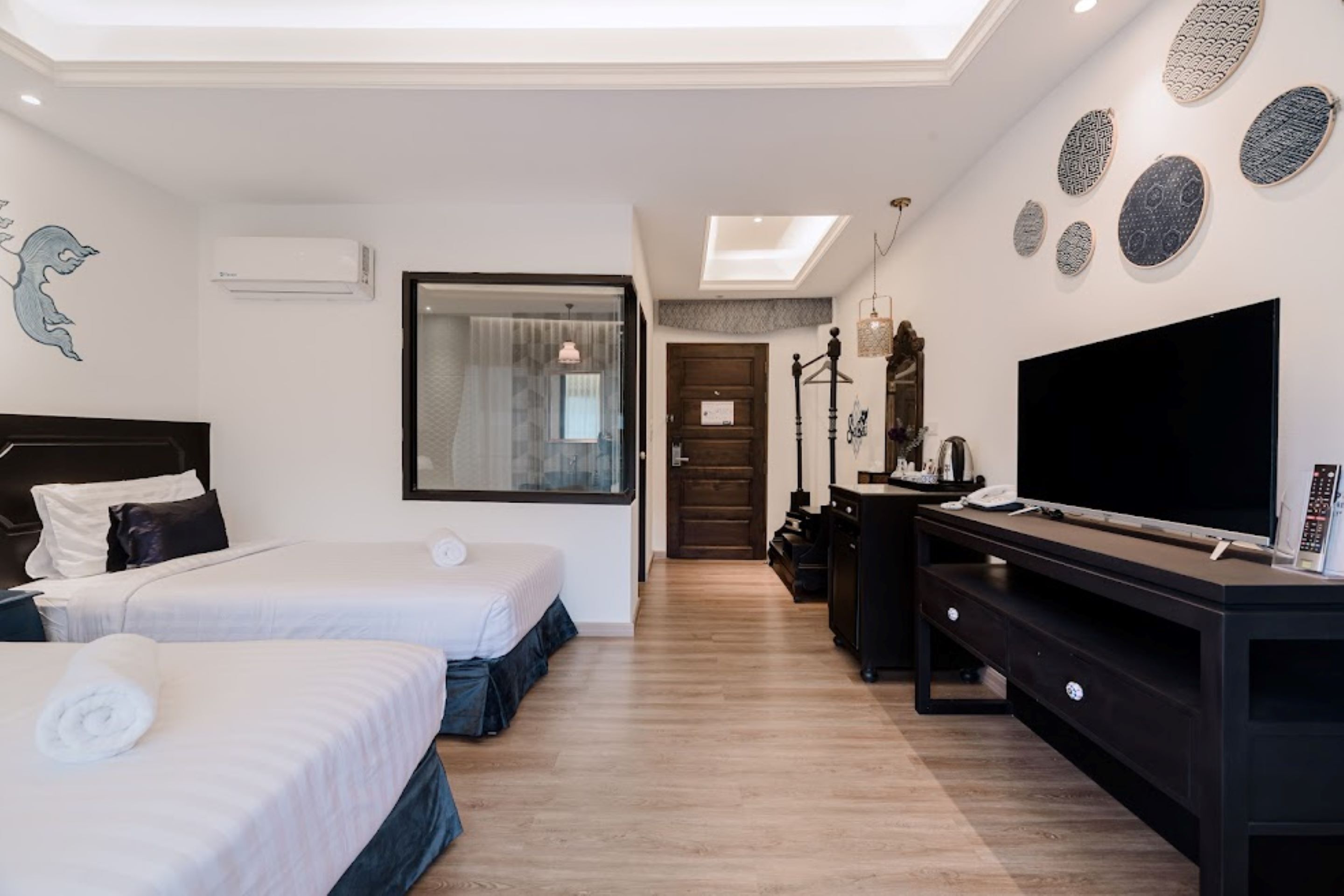 A hotel room with two beds, a TV, a desk, and a large window.