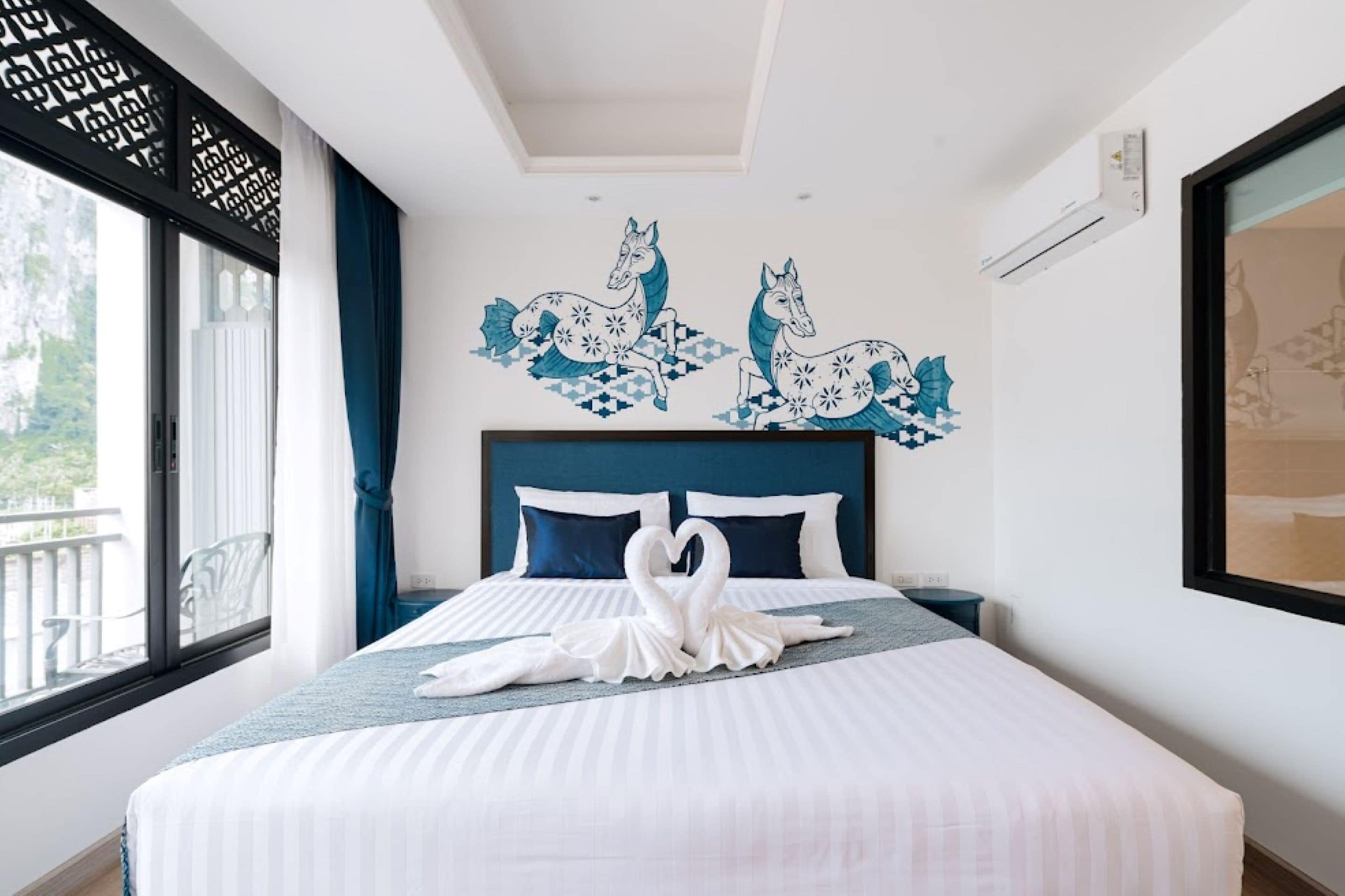Habitación de hotel con una cama grande, un mural decorativo, una ventana con vistas y una mesita de noche.